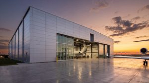 A modern airplane hangar construction featuring a large steel-framed structure with a private jet inside, designed for aircraft maintenance hangar operations.