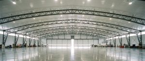 "A large, modern airplane hangar interior with multiple private jets parked inside, featuring polished concrete floors and structural steel framing, showcasing considerations for private plane hangar cost in aviation facility planning."