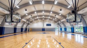 Spacious metal building basketball gym interior with arched steel roof and polished wooden court floor