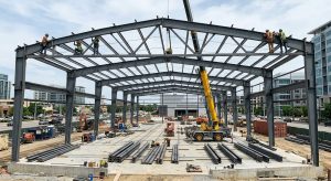 Workers are assembling the massive steel-structure framework of the exhibition hall with the aid of cranes; the site is tidy.