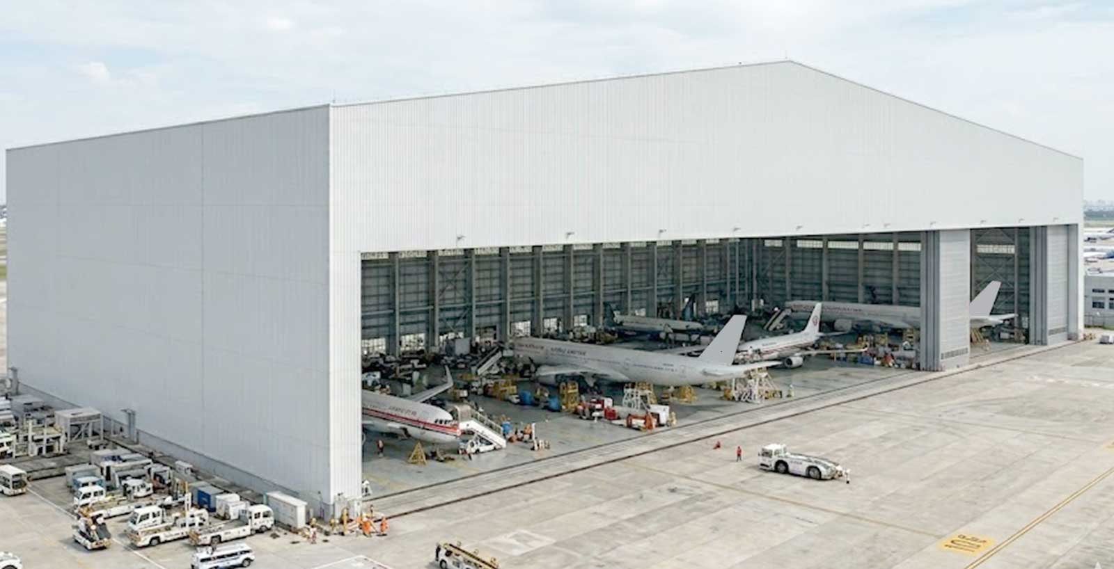 Large aircraft maintenance hangar with multiple commercial jets positioned inside for inspection and service operations.
