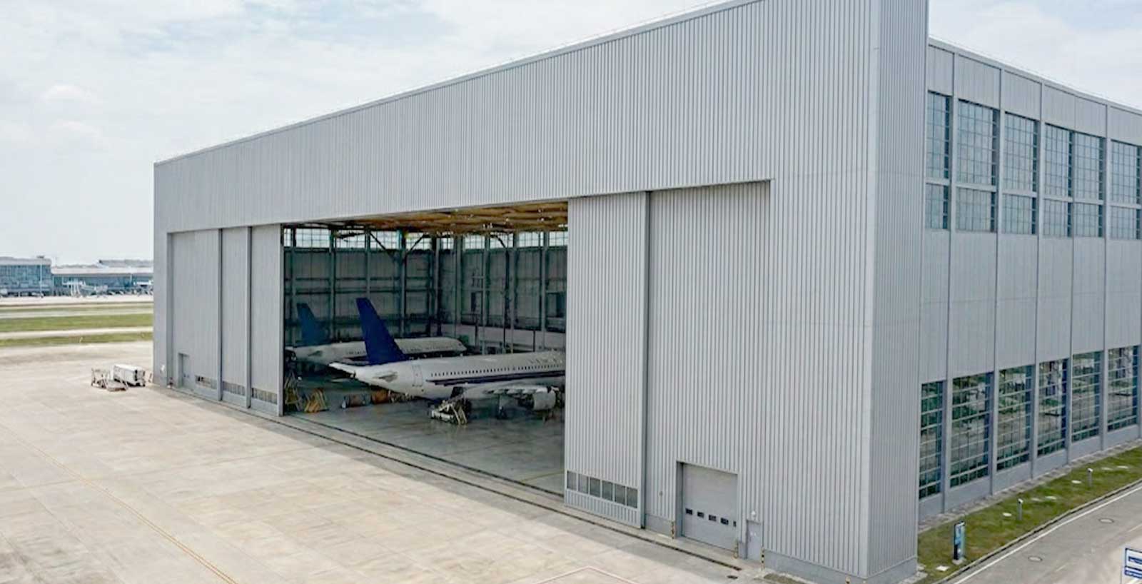 Large commercial aircraft hangar with several passenger jets inside a wide open bay for maintenance operations.