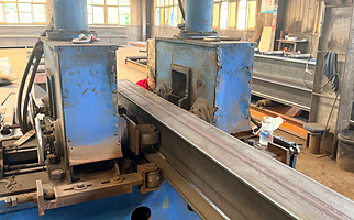 H-section steel beam passing through a straightening machine in the structural steel fabrication workshop.