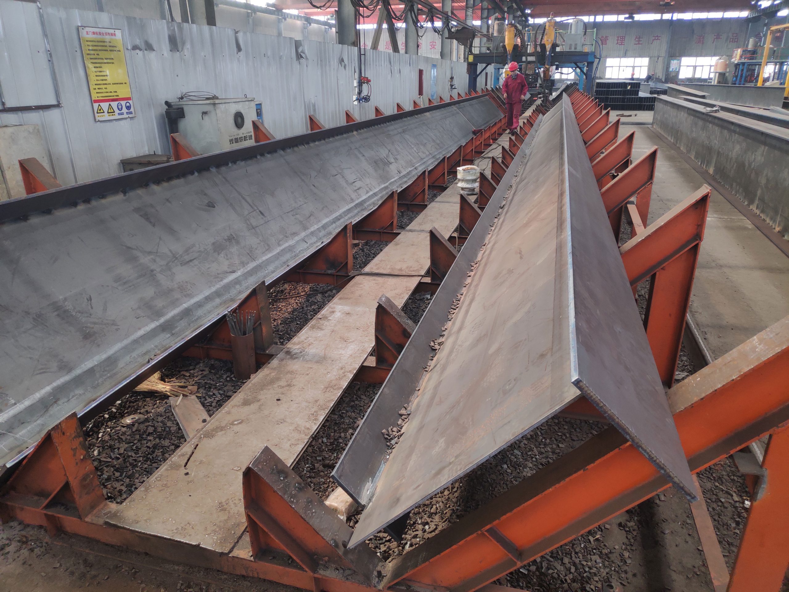 H-section steel beams positioned on welding fixtures during the submerged arc welding process inside a steel fabrication workshop.