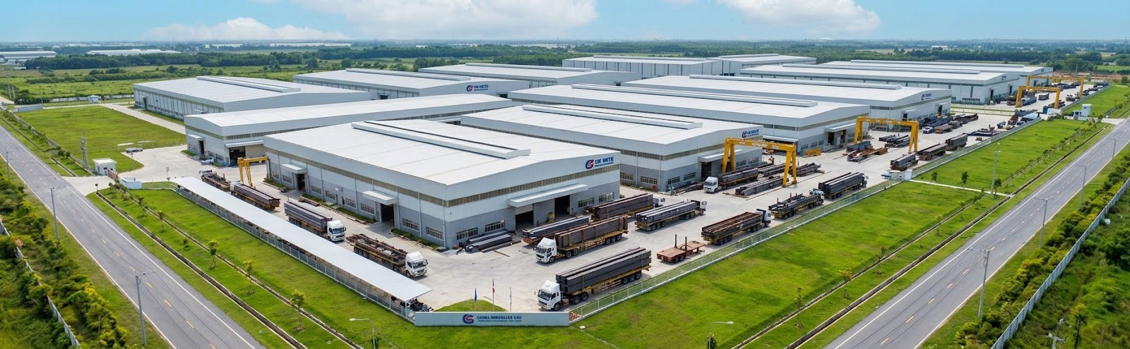 Aerial view of a large steel structure warehouse complex with multiple factory buildings, trucks, and outdoor gantry cranes.
