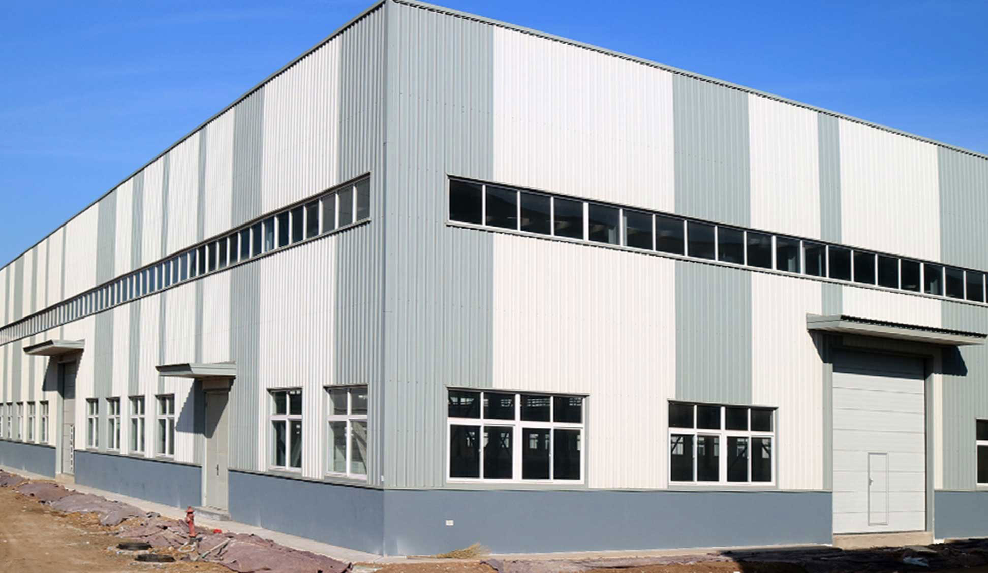 Industrial steel structure warehouse with metal wall cladding, ribbon windows, and a large overhead loading door.