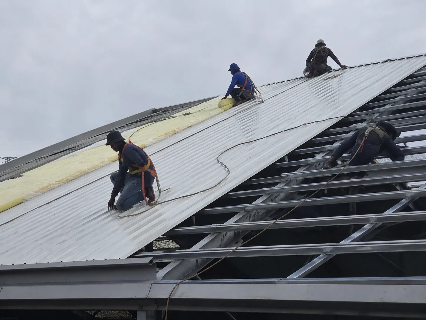 Workers installing glass wool insulation and steel roof panels on the 4,320 m² Bolivia warehouse.