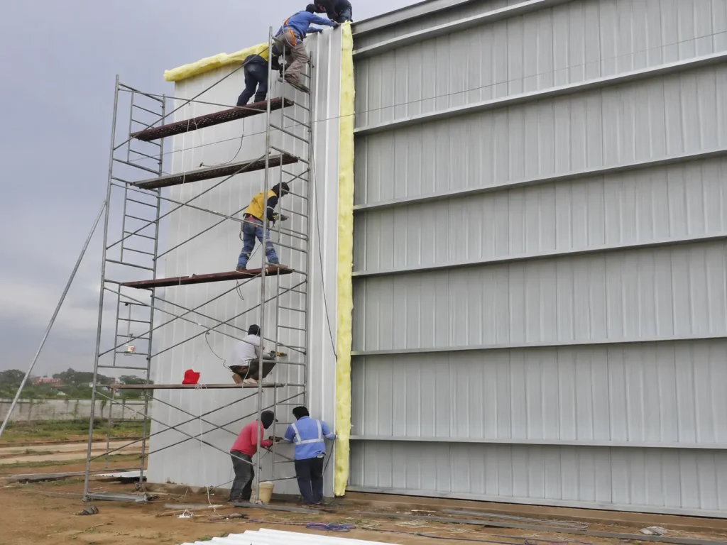 Workers installing glass wool insulation and steel wall panels on the 4,320 m² Bolivia warehouse.