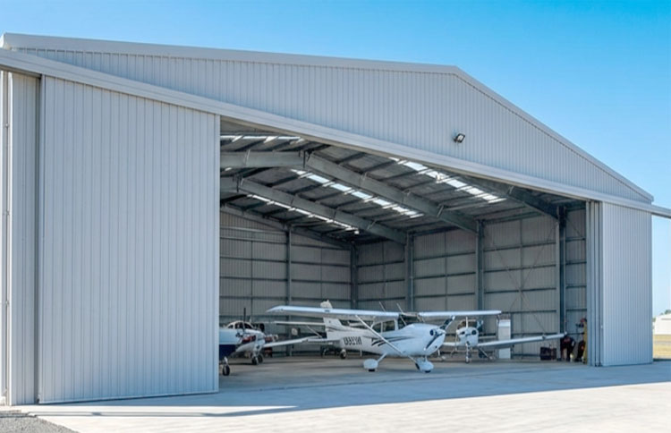 Light aircraft hangar with several small propeller planes parked inside behind a wide open sliding door.