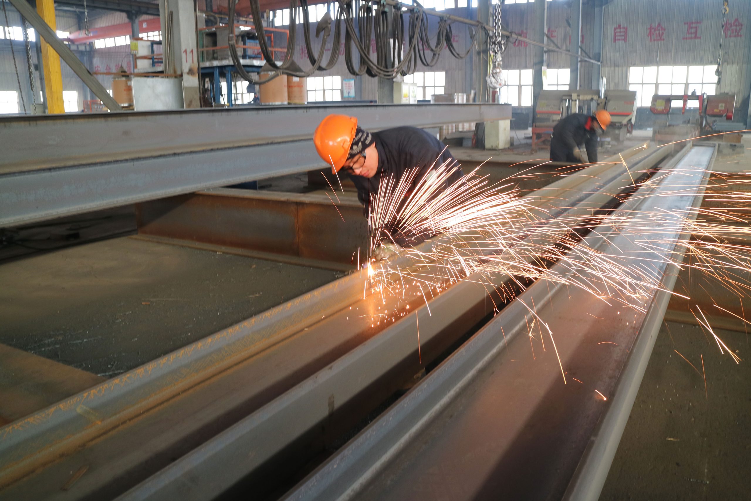 Workers grinding H-section steel beams to smooth fabricated surfaces during the steel structure building process.