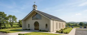 Modern metal church building with vertical wall panels, pitched roof, arched windows, and a cross-topped steeple for rural worship projects.