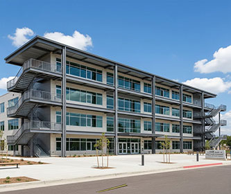 Four-storey steel structure school building with large windows, covered balconies, multiple entrances, and external staircases.