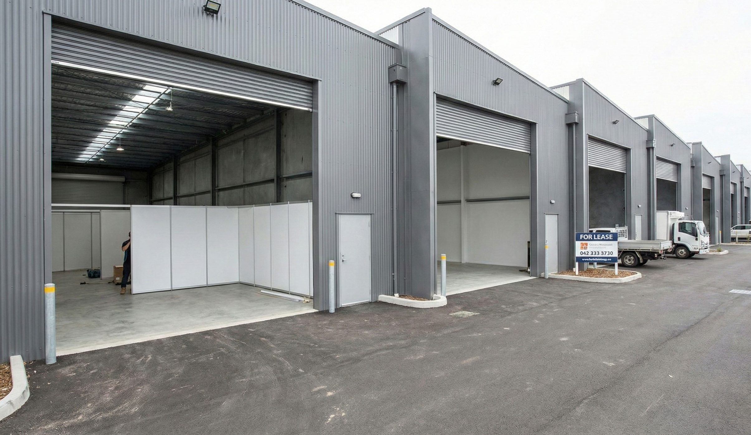 Multi-unit steel structure storage warehouse with roller shutter doors, pedestrian entrances, and separate loading bays.