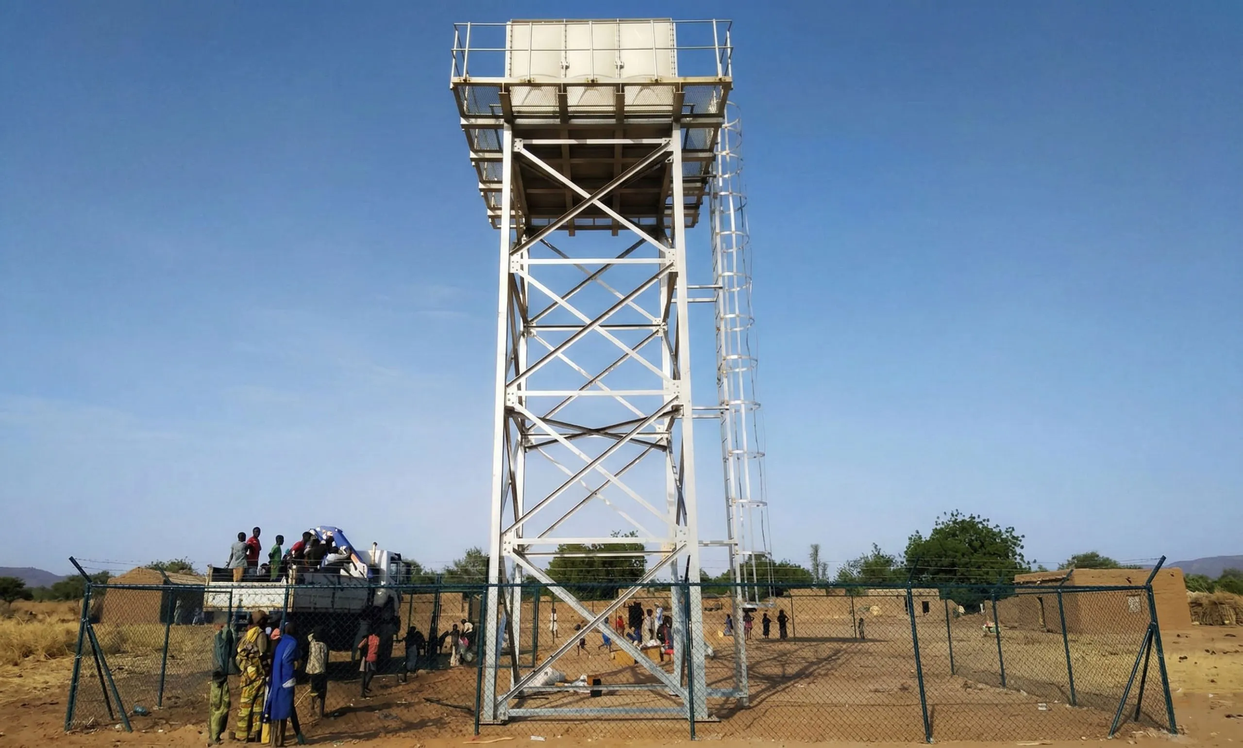 Lattice steel water tower with an elevated tank, cross bracing and access ladder at a rural site in Niger.