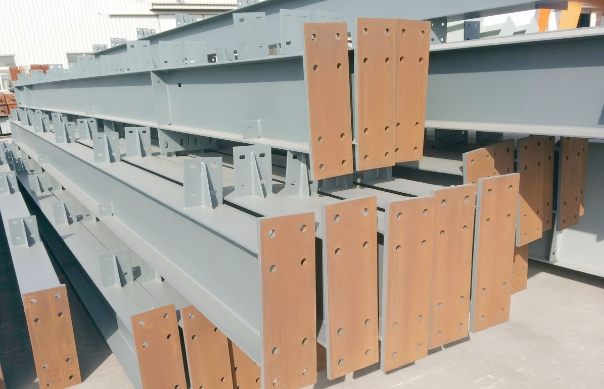 Painted H-section steel members with drilled end plates and welded connection brackets stacked for steel building assembly.