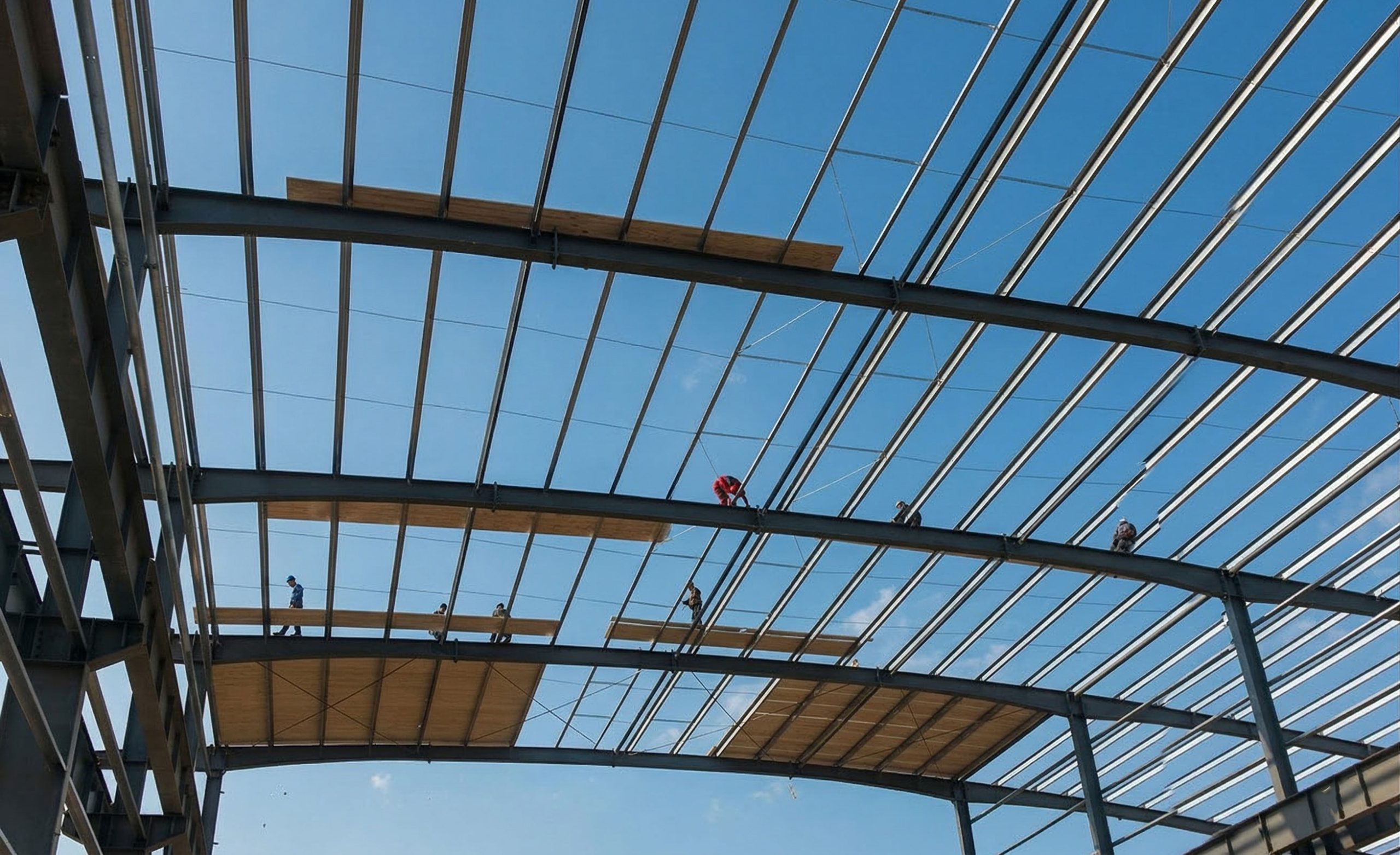 Workers using temporary timber walk boards on roof purlins while preparing for steel structure building roof panel installation.