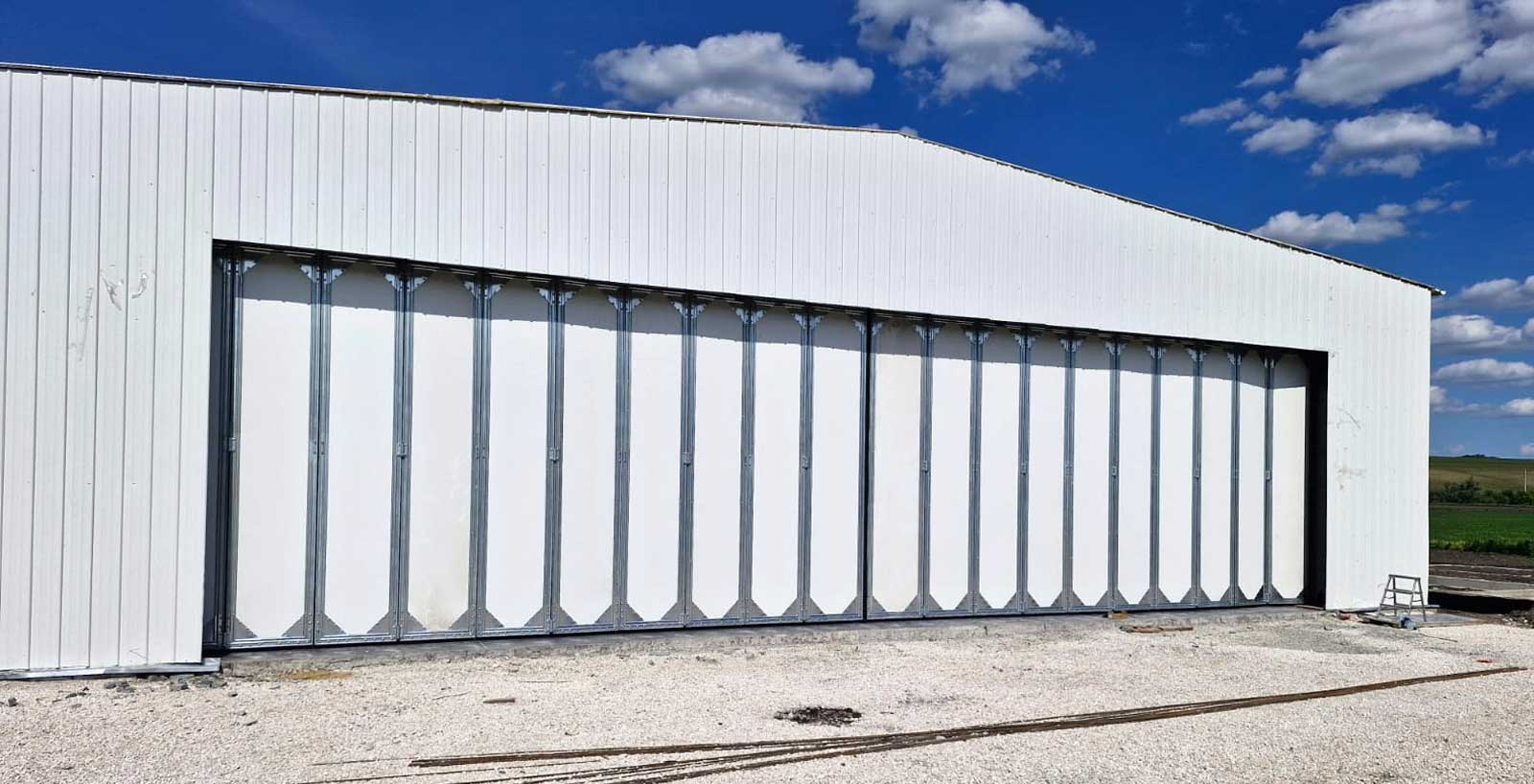 Multi-panel sliding aircraft hangar doors installed across the wide entrance of a white steel hangar building.