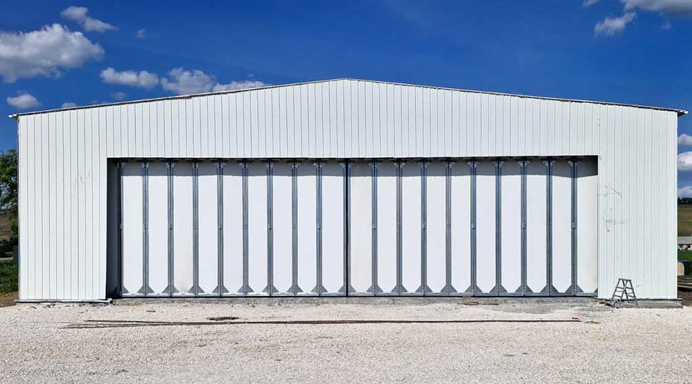 Steel aircraft hangar with closed multi-panel sliding doors across a wide entrance and white metal wall cladding.