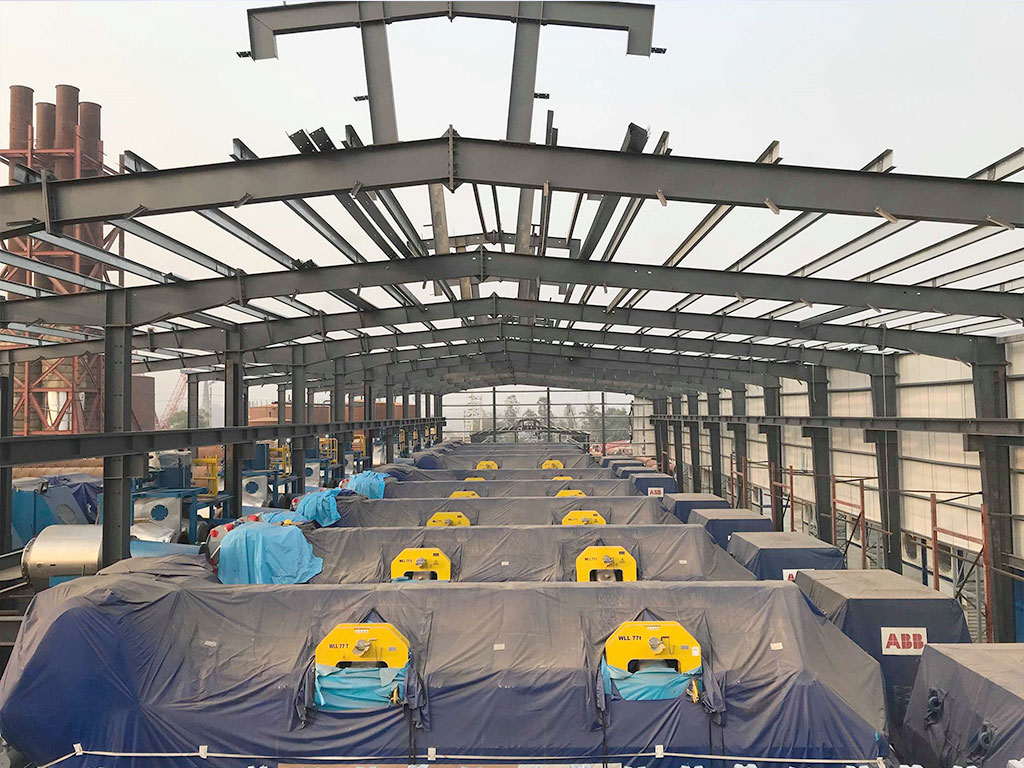 Steel structure factory building project in Bangladesh with portal frames, roof purlins, and industrial equipment installed inside.