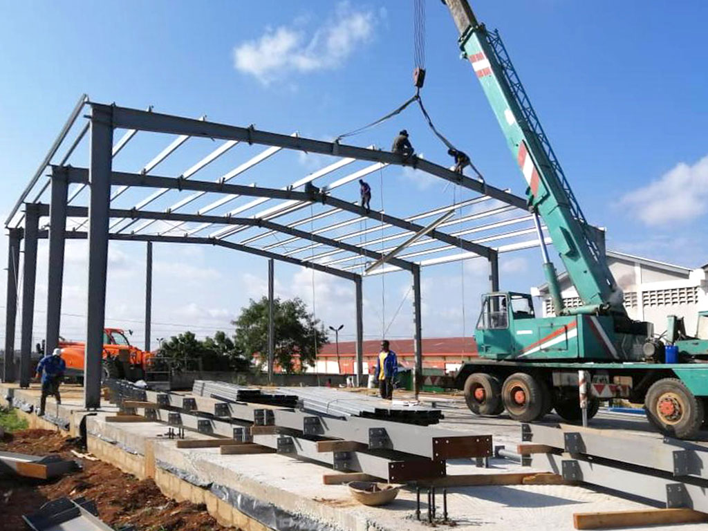 Steel structure industrial building project in Ghana with portal frames, roof purlins, bracing, and crane-assisted erection.