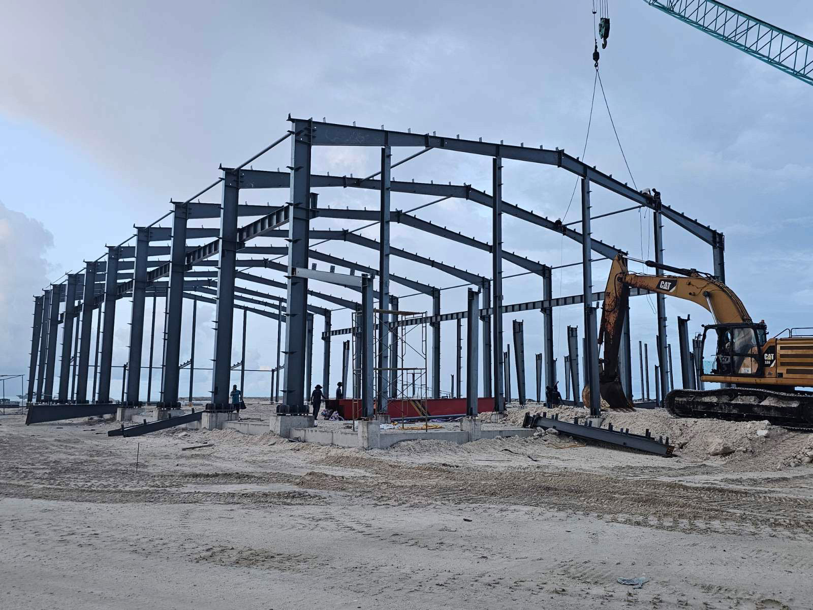 Steel structure industrial building project in Maldives with portal frames, steel columns, roof rafters, and crane-assisted erection.