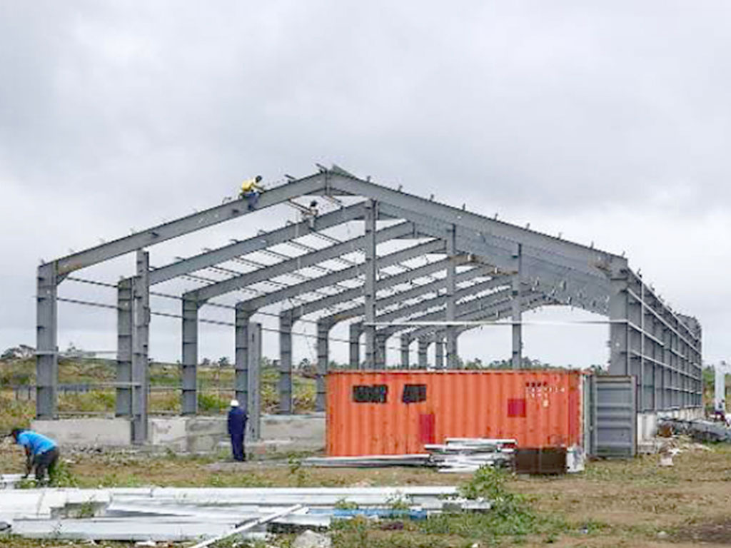 Steel structure industrial building project in Mauritius with portal frames, roof purlins, wall girts, and workers during erection.