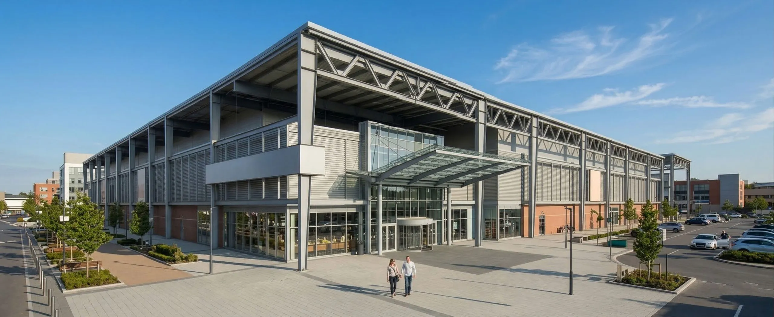 Shopping mall exterior with exposed steel frame, glass entrance canopy, and parking area for retail projects