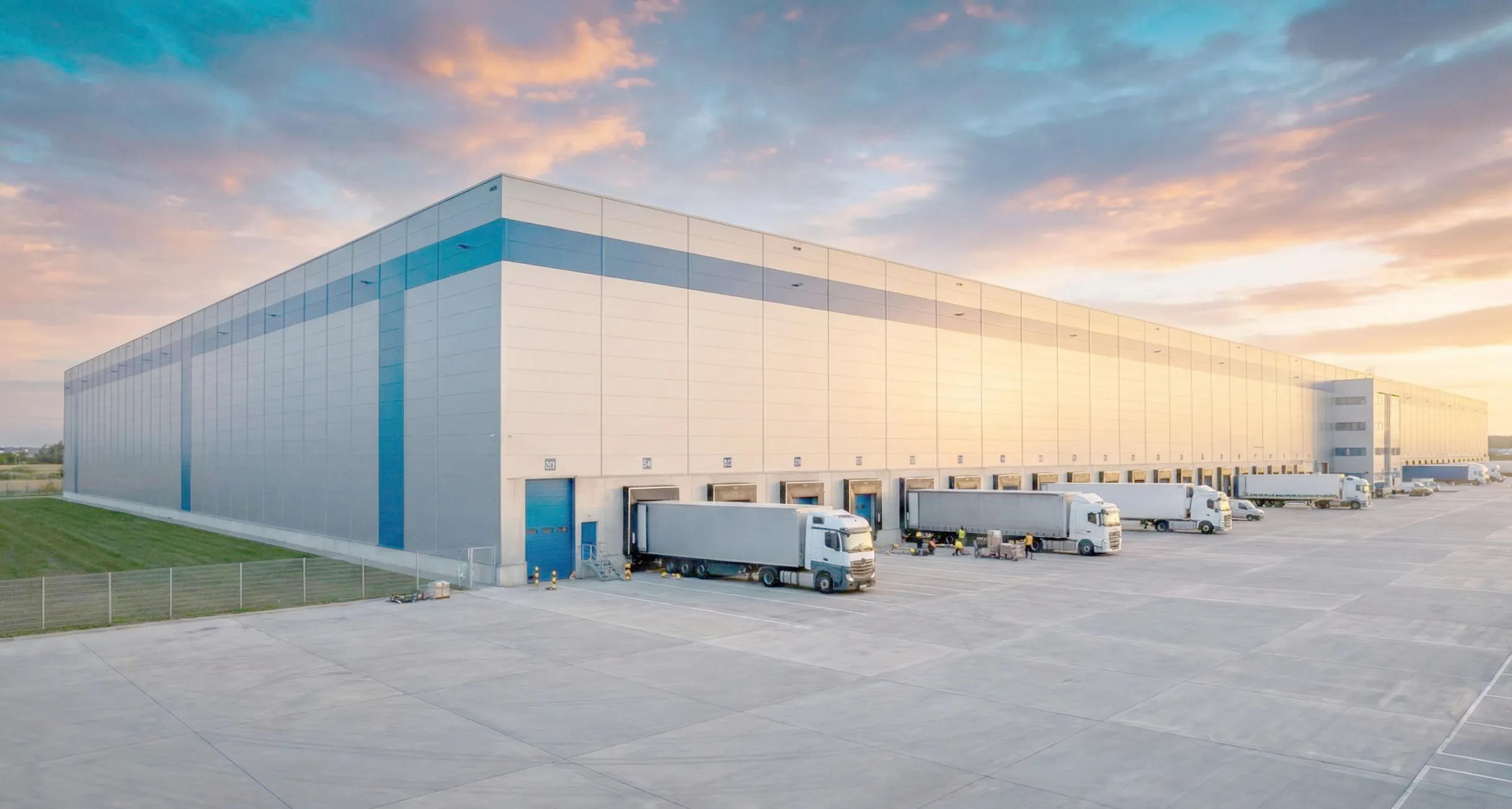 Steel workshop building exterior with metal wall panels, loading dock doors, truck access, and large industrial yard.