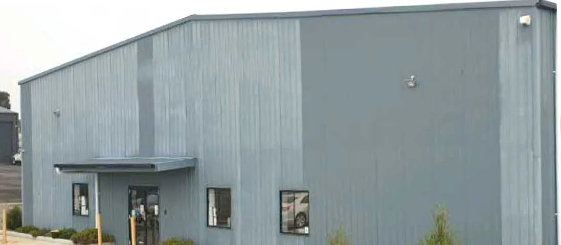 Steel workshop building exterior with grey metal wall panels, entrance canopy, windows, and industrial workshop facade.
