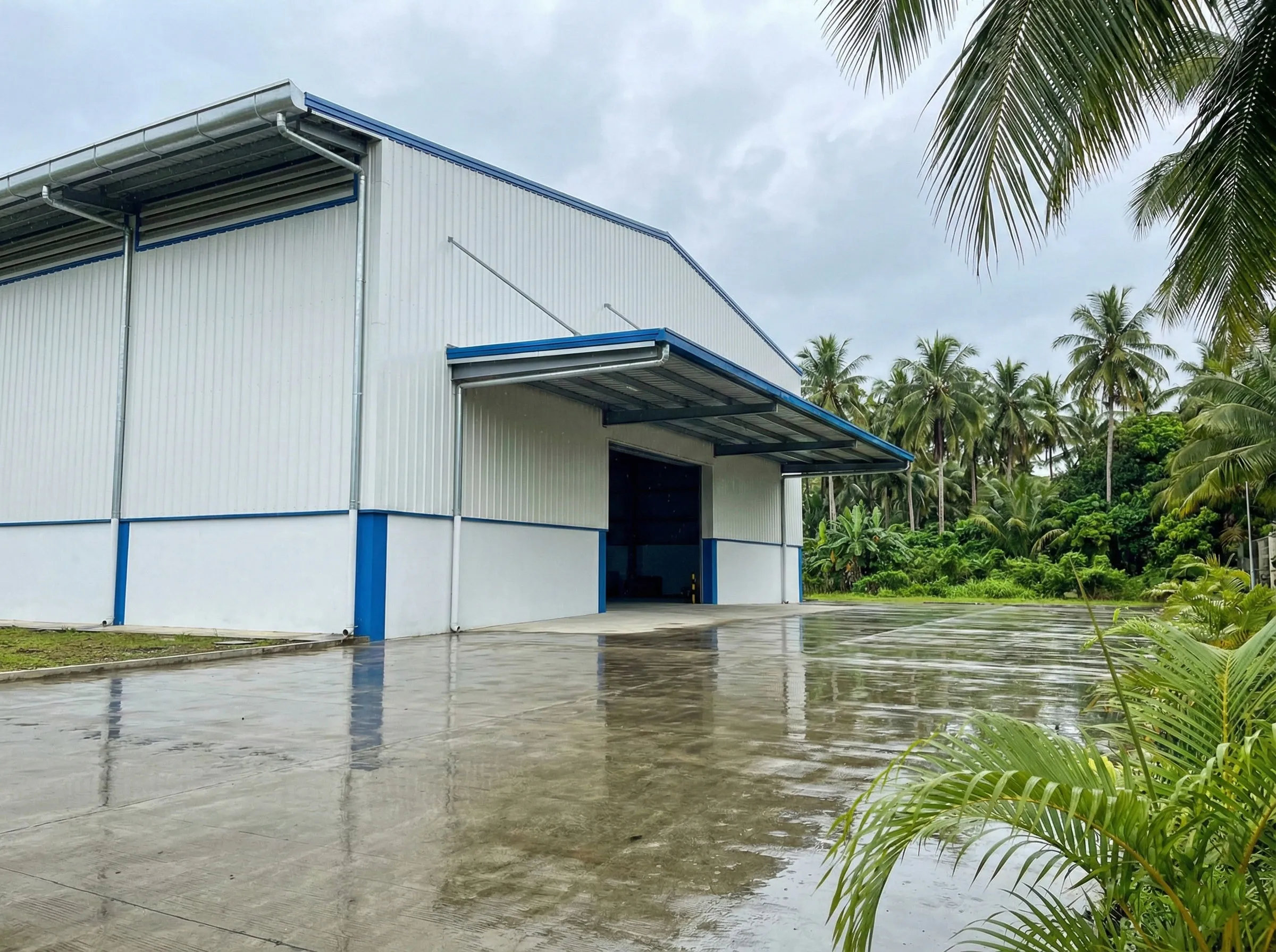 Steel workshop building exterior with metal wall panels, roof canopy, gutter drainage, downpipes, and wide access opening.