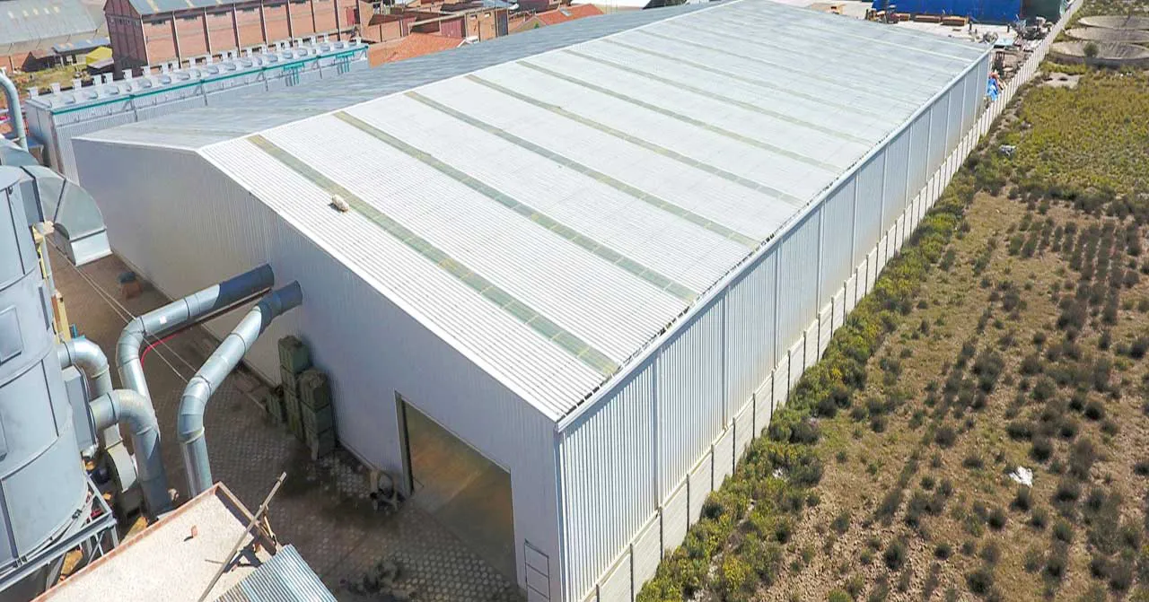 Steel workshop building with metal roof panels, skylight strips, wall cladding, side ventilation ducts, and wide access opening.