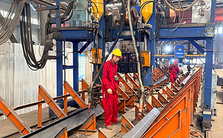 Submerged arc welding of H-section steel beams on an automated line in the structural steel fabrication workshop.