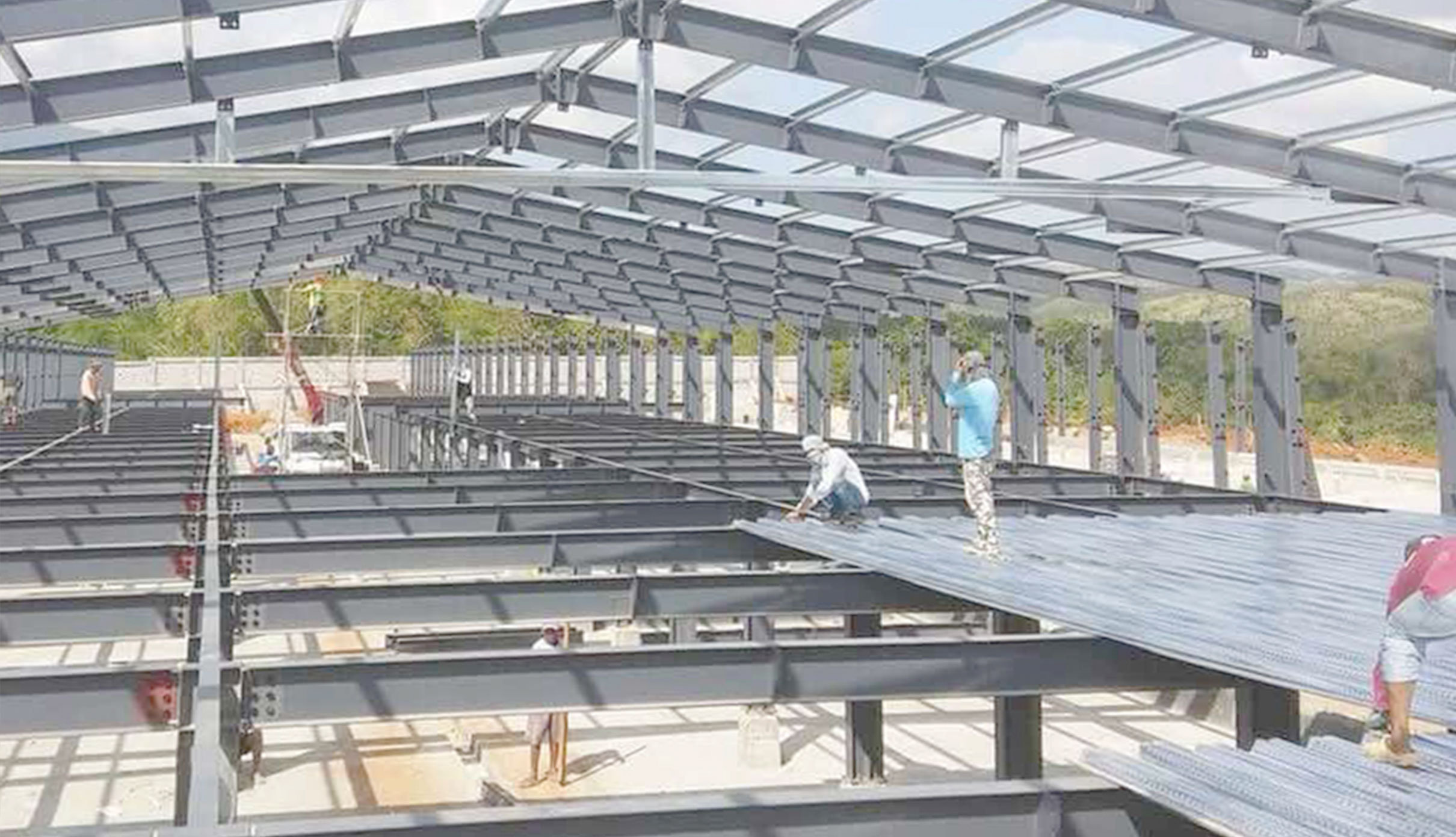 Workers installing metal floor decking inside a two-story steel frame chicken house under construction.