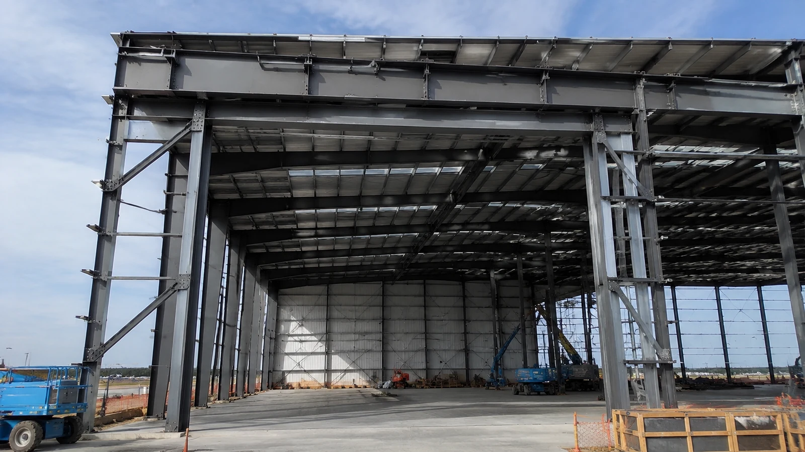 Steel header, jamb columns, and bracing frame a large aircraft hangar opening under construction.