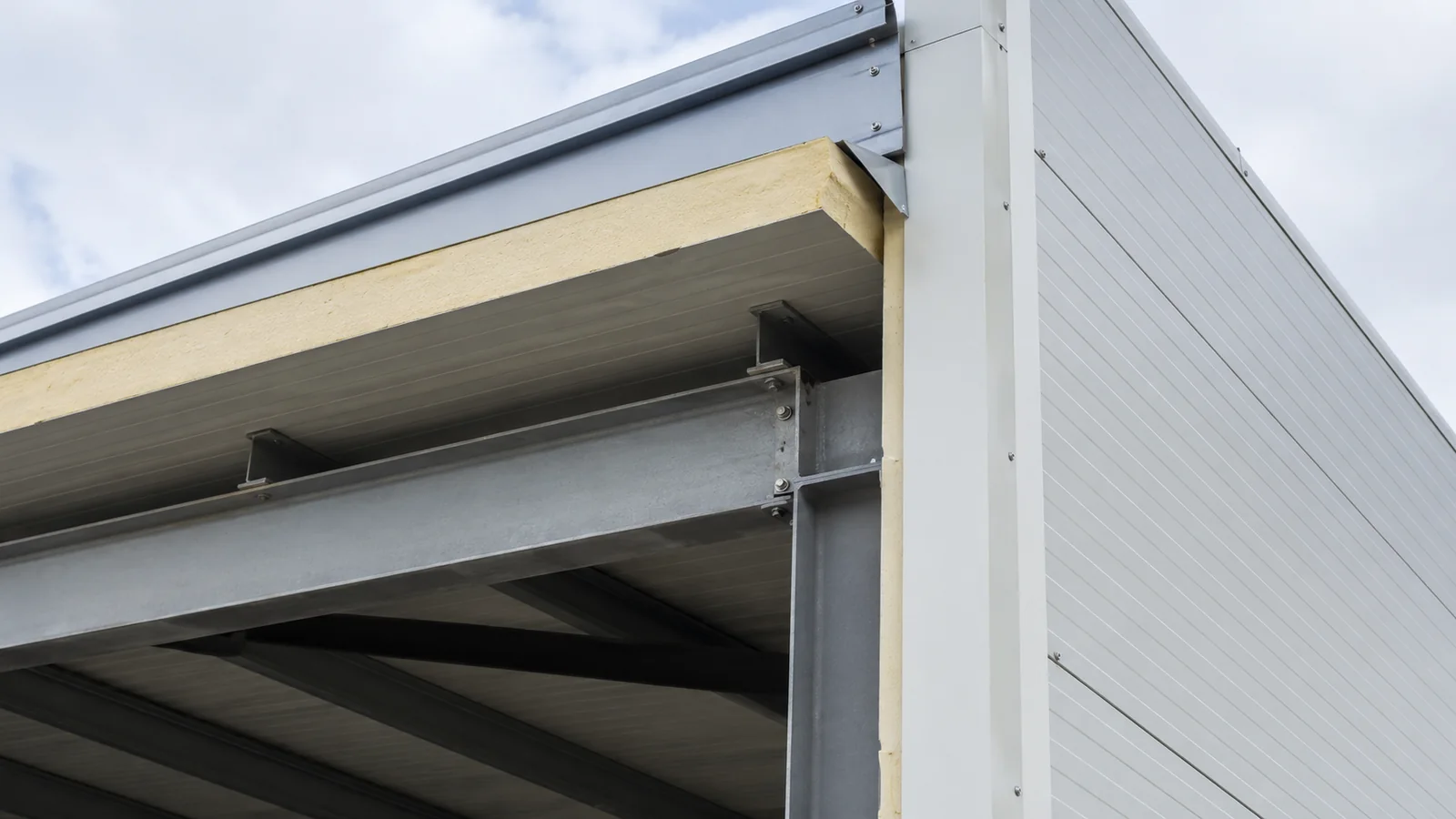 Exposed insulated roof panel edge and steel eave framing show the roof-to-wall connection.