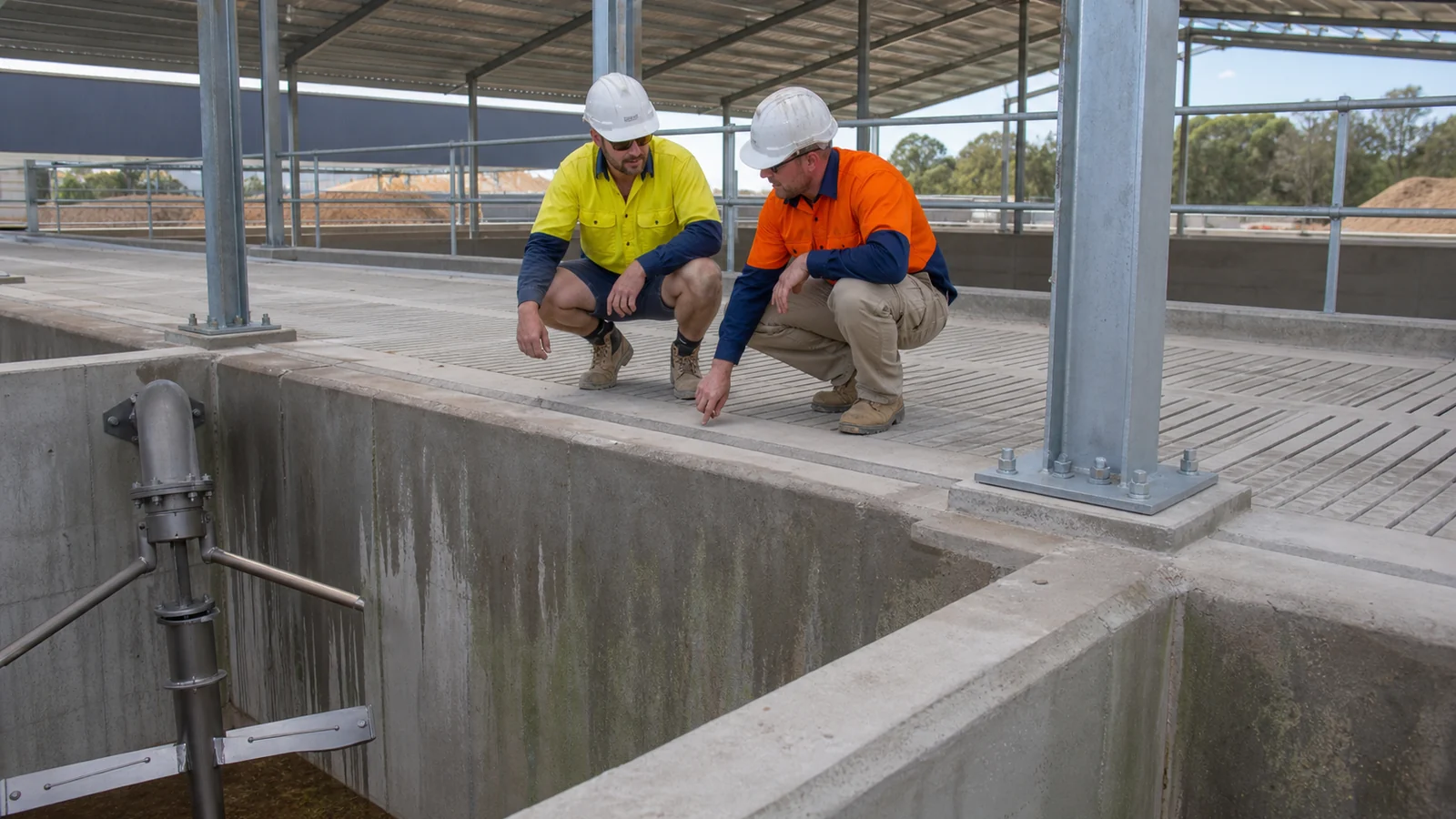 Workers inspect slat supports, concrete slurry tank walls and steel column bases in a sheep shed.