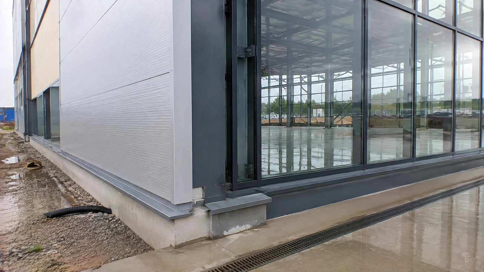 Glass-to-panel corner, sill flashing, and perimeter drainage at a steel showroom facade.