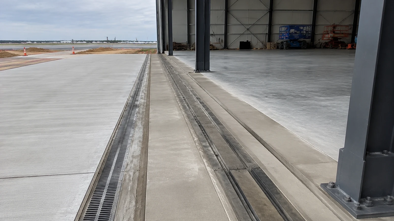 Recessed hangar door tracks and apron drainage run across the concrete threshold.