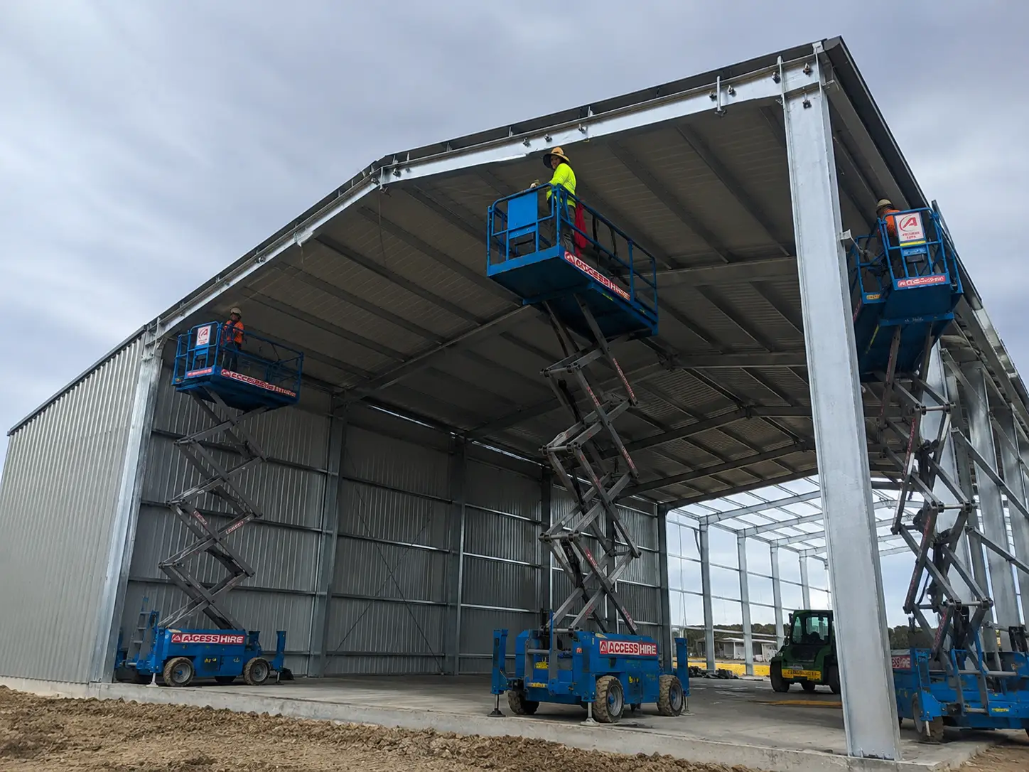 Australia farm warehouse under construction with steel frame and workers installing roof panels