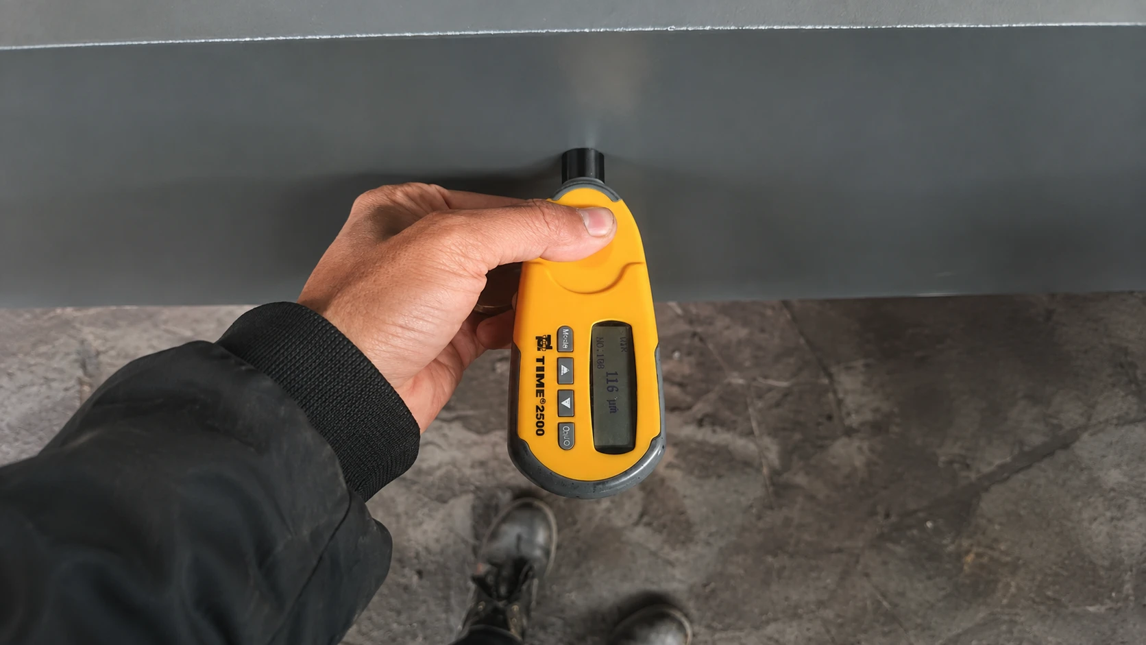 Inspector measuring protective coating thickness on a fabricated steel structure component using a digital coating gauge.