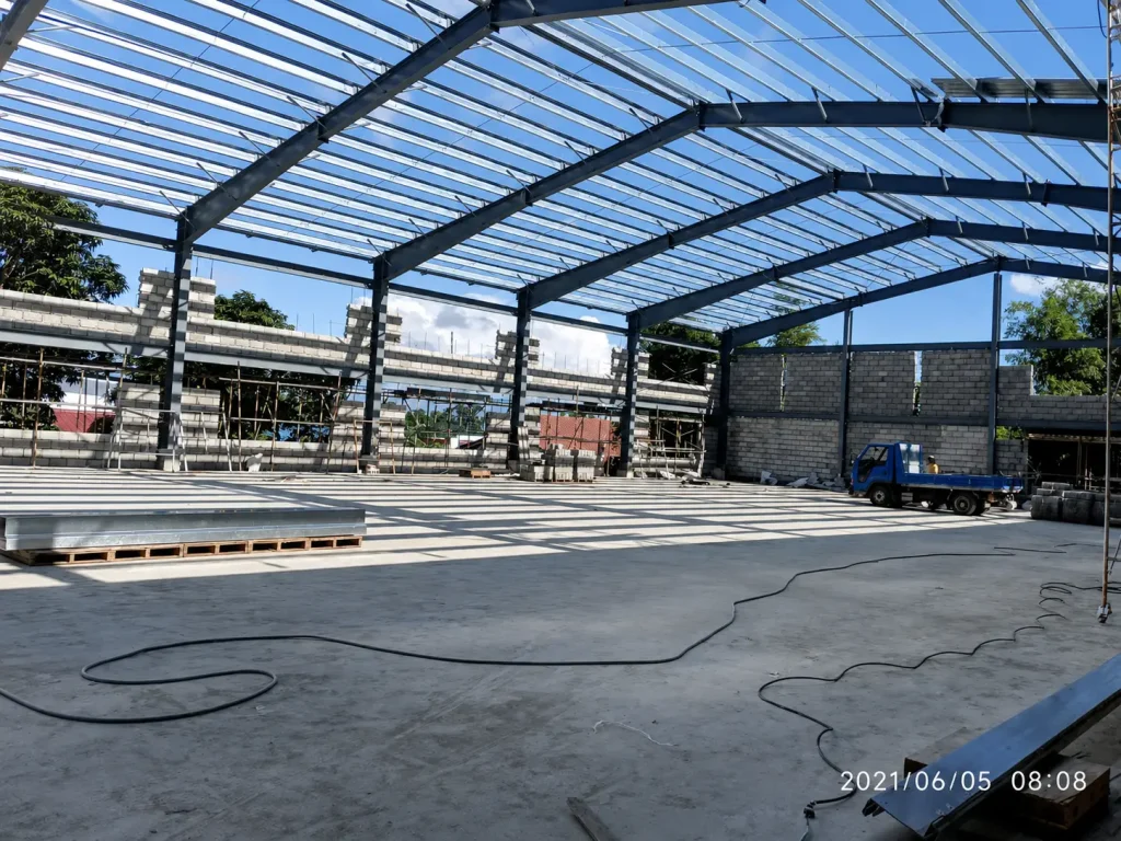 Philippines steel warehouse interior during construction, showing portal frames, roof purlins, wall work and site materials.