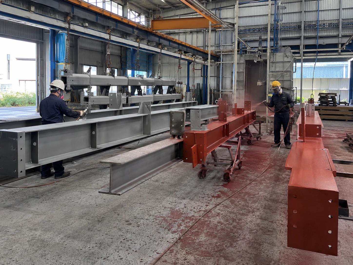 Workers apply protective coating to fabricated steel beams for the Romania warehouse project inside the factory.