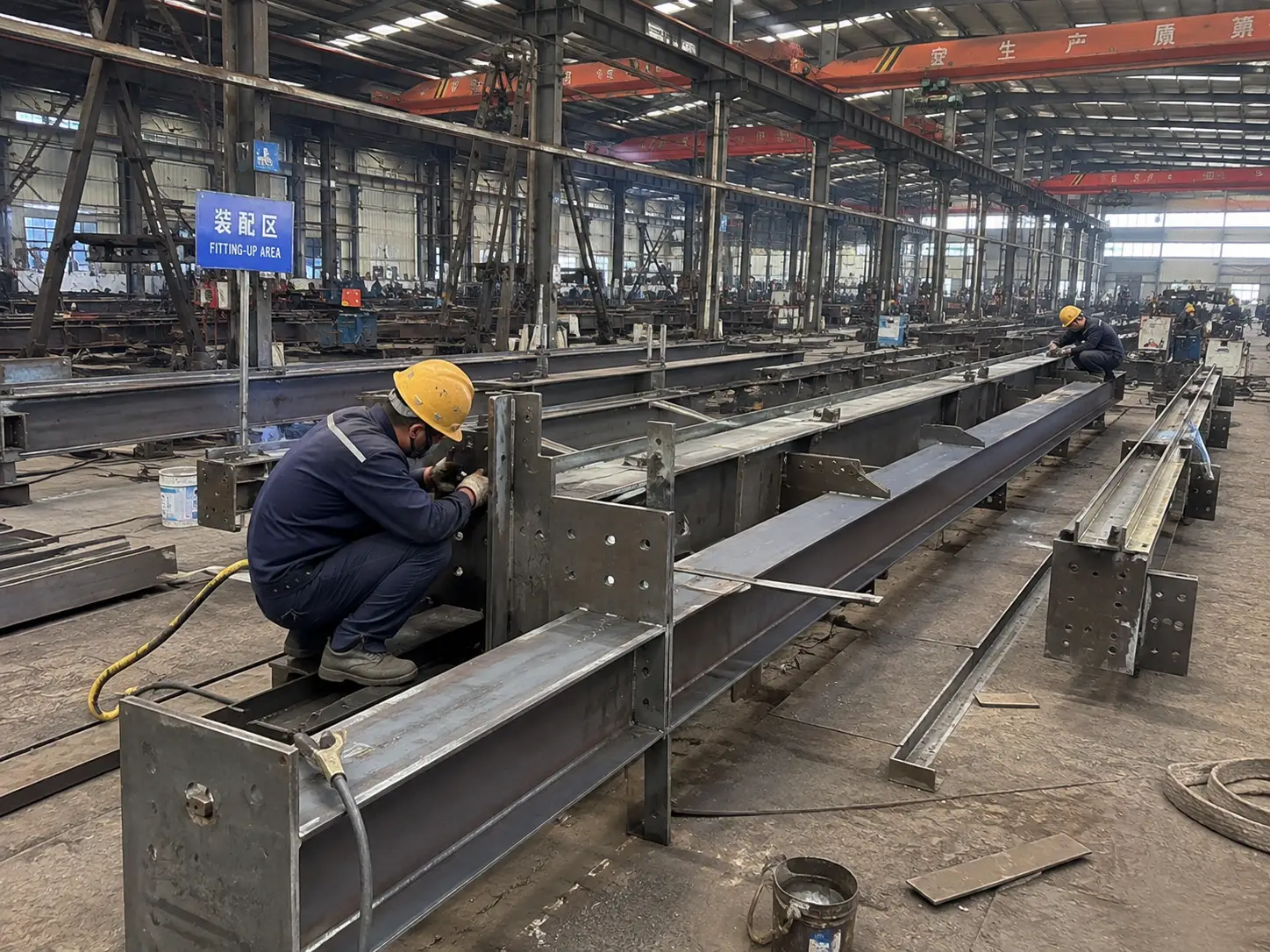 Steel beam fitting up process in fabrication factory with workers assembling structural components