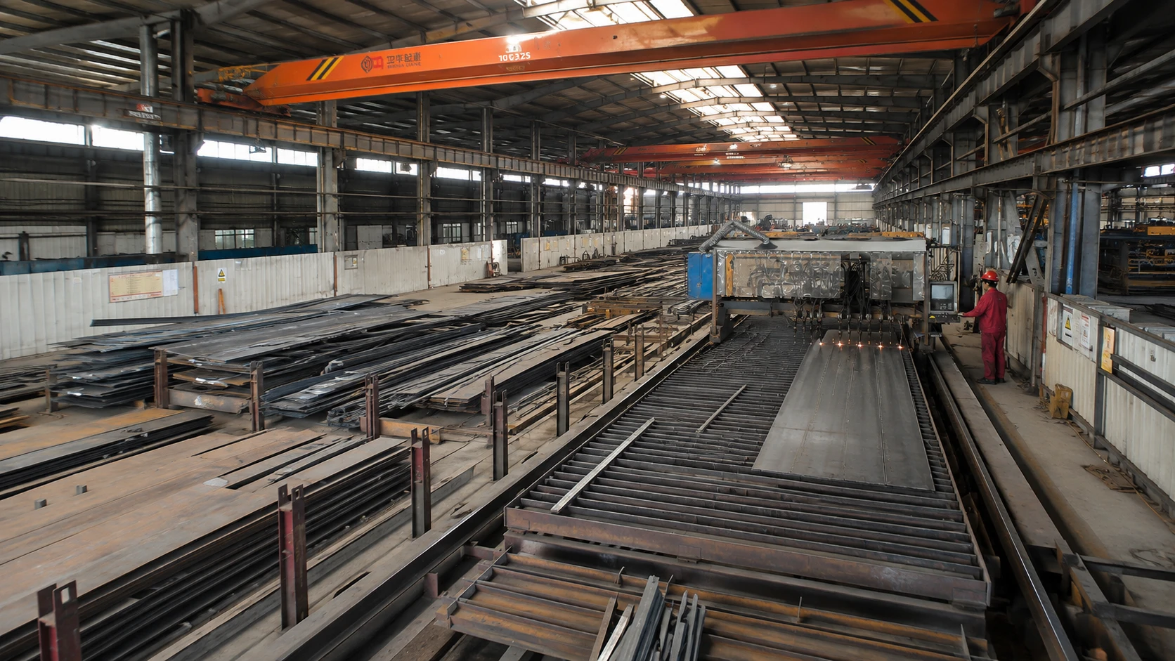 Steel structure production workshop with CNC plate cutting equipment, overhead cranes and stacked steel plates.