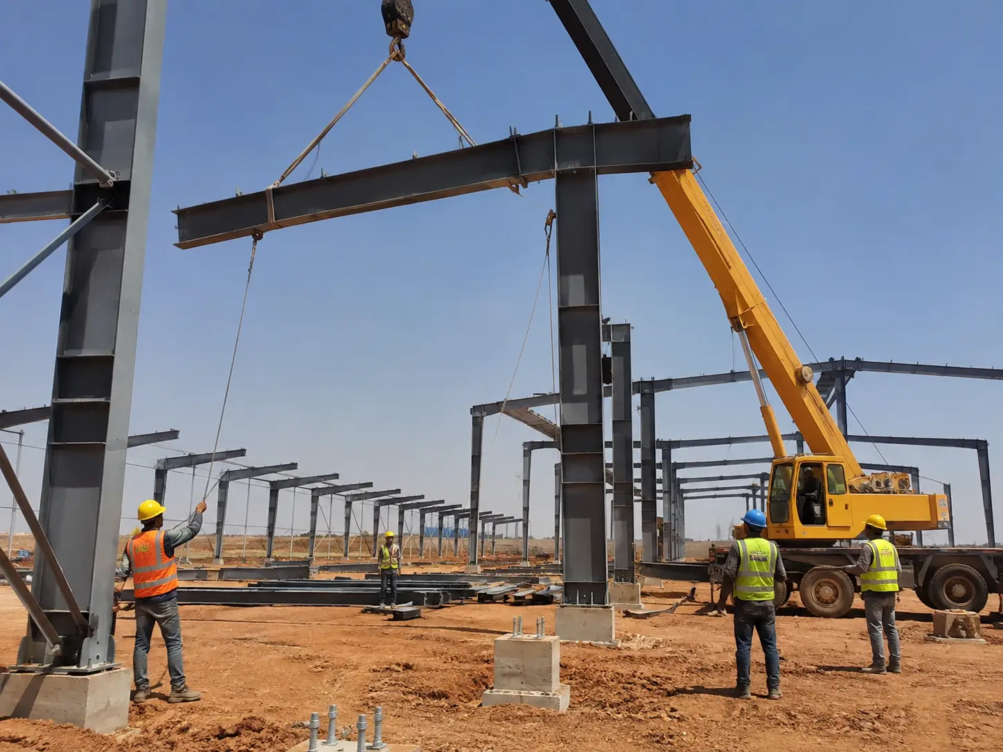 Steel warehouse main frame erection with crane lifting steel beams and workers guiding installation