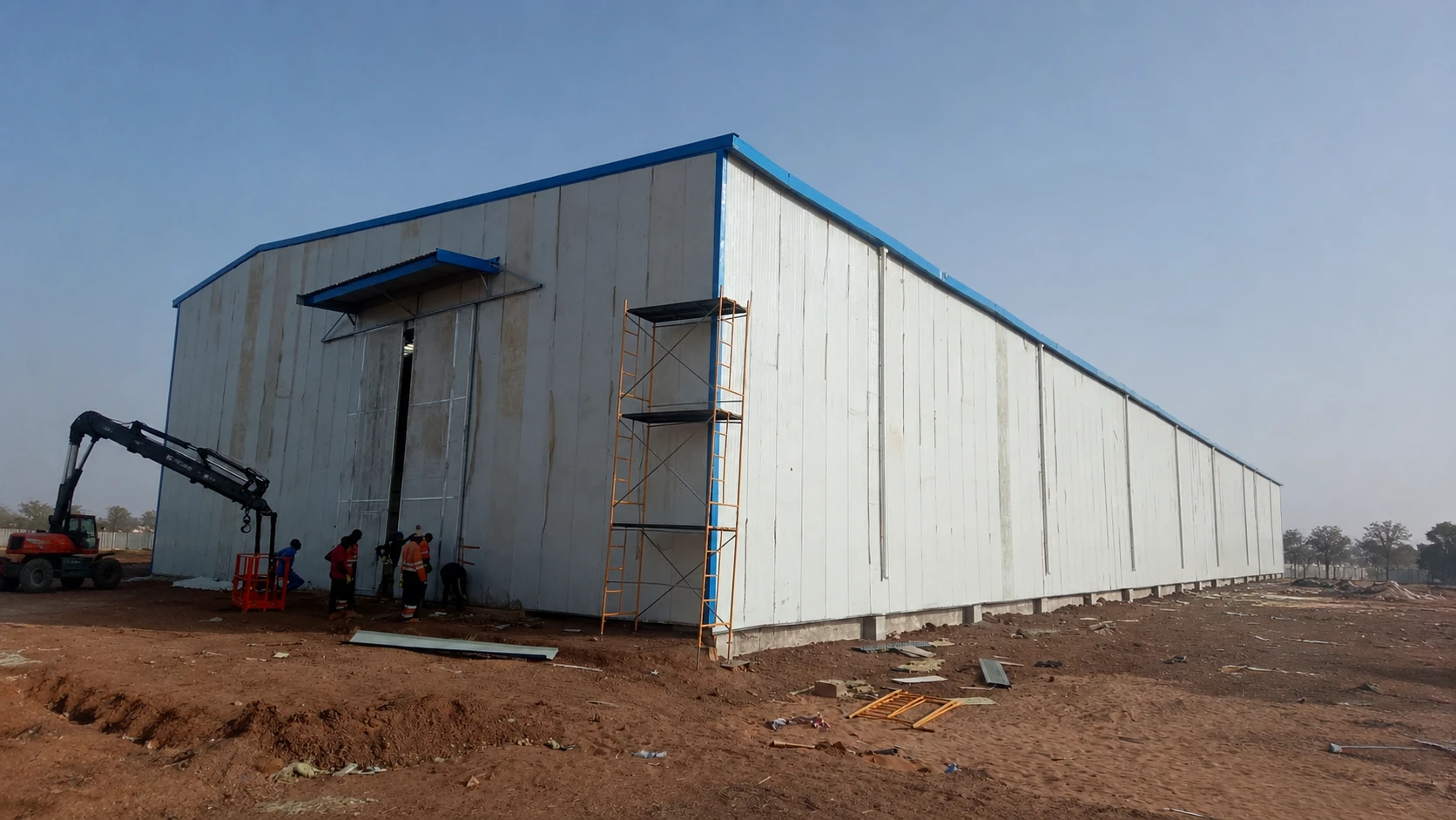 Steel structure warehouse with insulated wall panels, workers and scaffolding during exterior installation on site.