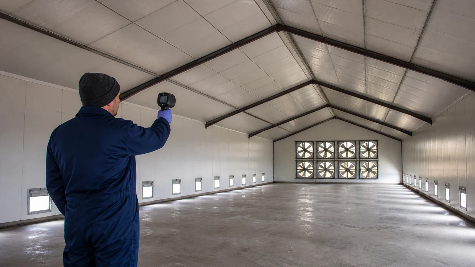Inspector scans insulated roof and wall joints with exhaust fans located only on the far gable.