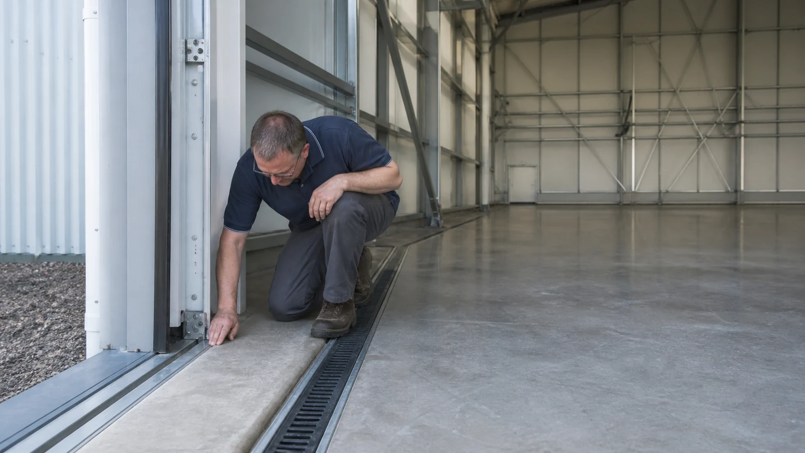 Inspector checks a hangar door track, floor joint, sealant, and drain interface