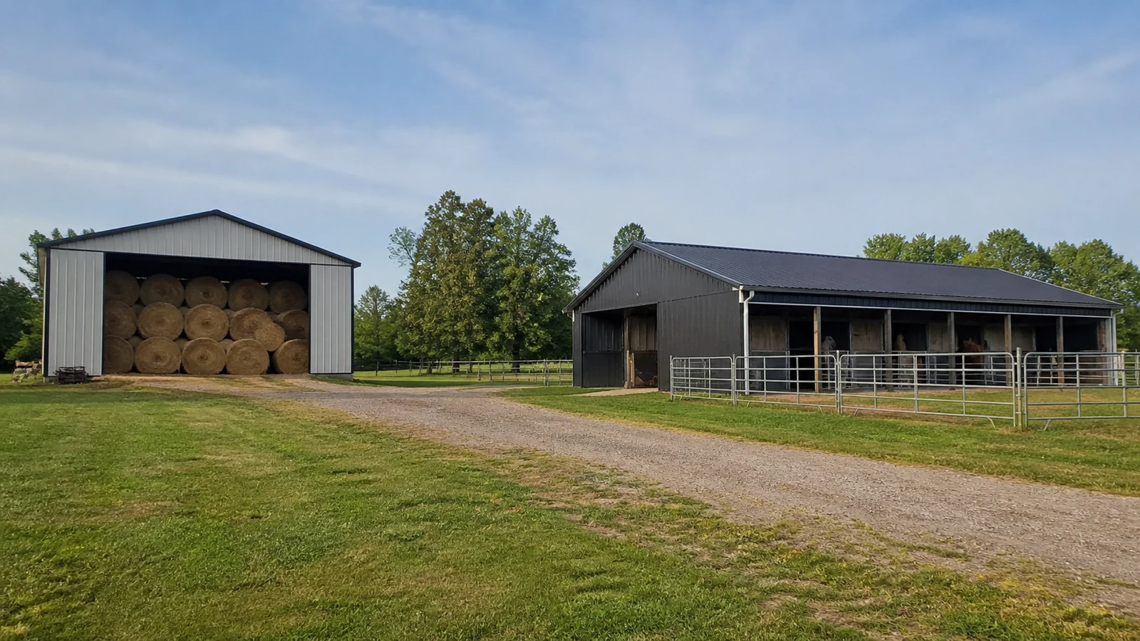 Detached hay storage stands apart from an occupied steel horse barn on a clear site