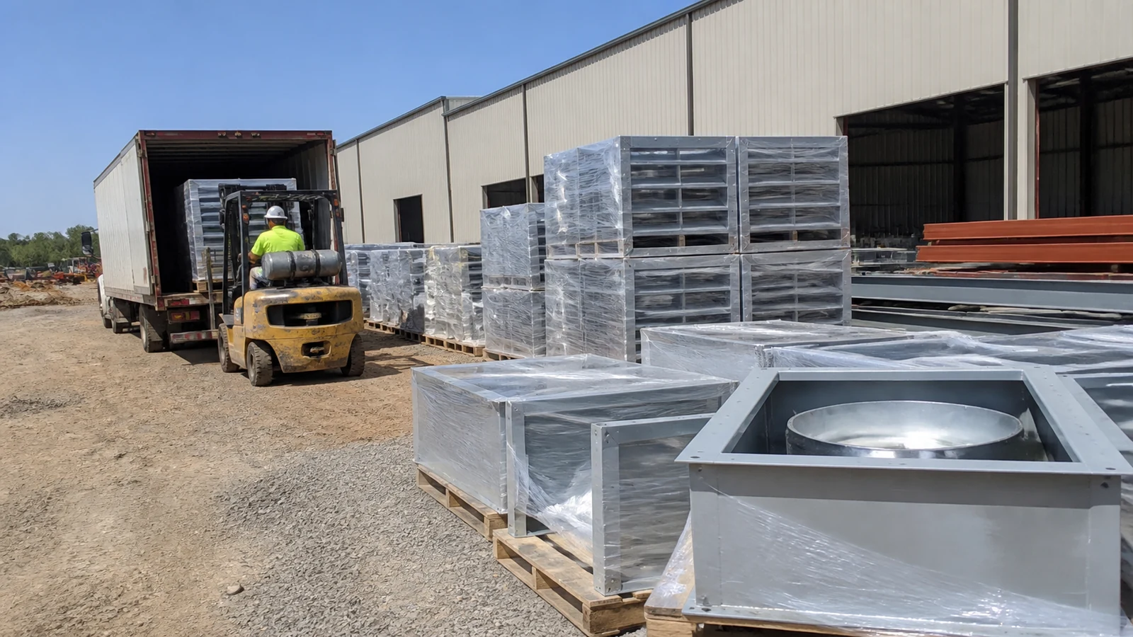 Fans, louvers, curbs, and steel framing arrive protected at a warehouse construction site.